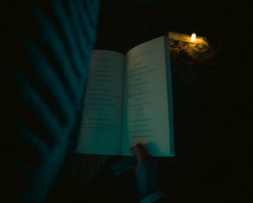 A person reading a physical book with a directed reading lamp in a dark room